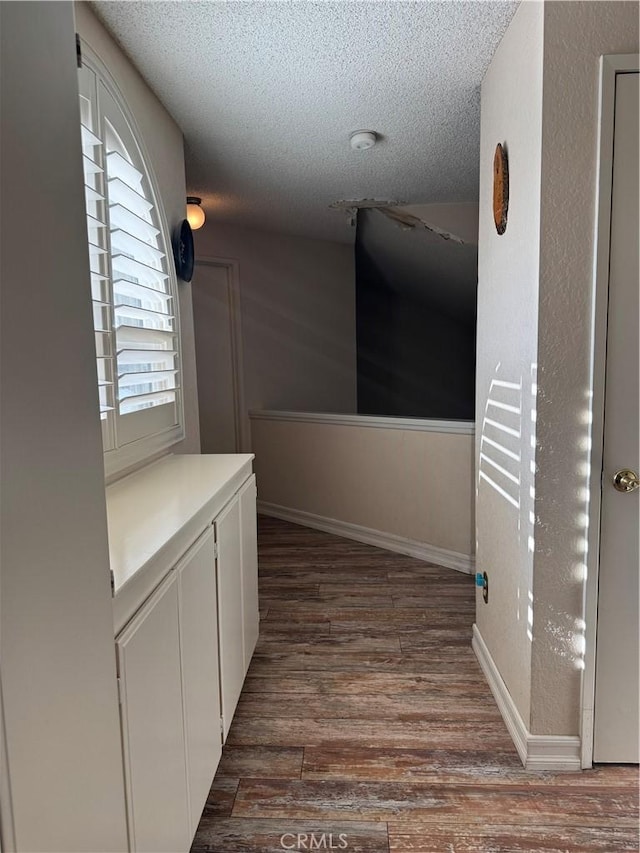 hallway featuring a textured ceiling, wood finished floors, and baseboards