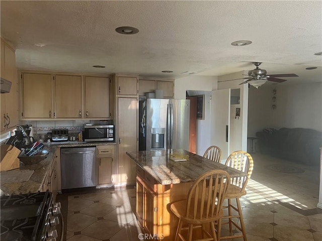 23680 Rhea Dr, Moreno Valley, CA 92557 - kitchen featuring a textured ceiling, ceiling fan, decorative backsplash, a kitchen island, and appliances with stainless steel finishes