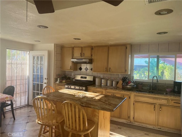 23680 Rhea Dr, Moreno Valley, CA 92557 - kitchen featuring a sink, dark stone counters, stainless steel gas range oven, backsplash, and under cabinet range hood