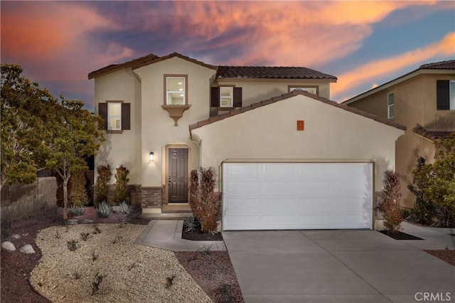 mediterranean / spanish-style house featuring an attached garage, concrete driveway, a tiled roof, and stucco siding