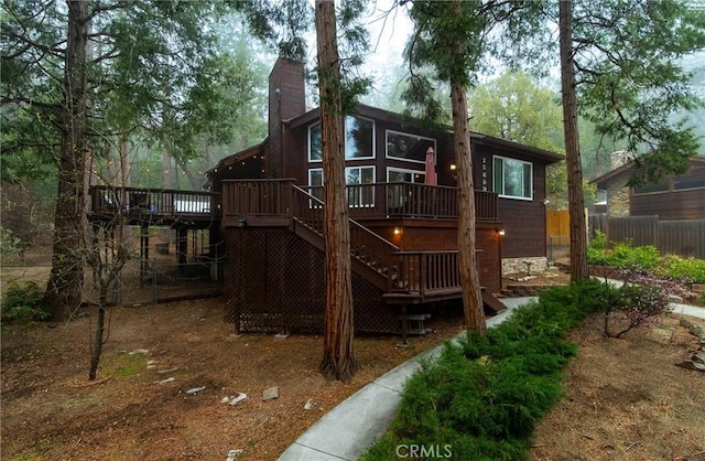 rear view of house with fence, a wooden deck, a chimney, and stairs