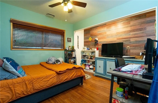 bedroom with wooden walls, ceiling fan, wood finished floors, and visible vents
