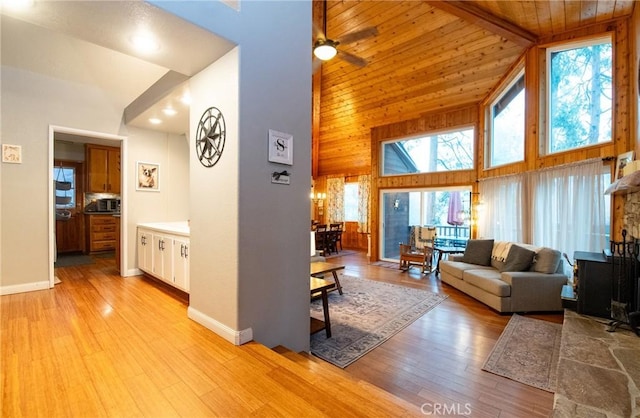 living room with wood walls, light wood-type flooring, baseboards, wood ceiling, and high vaulted ceiling