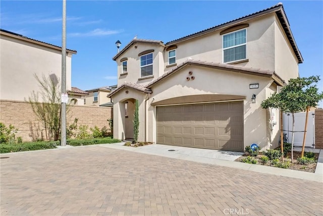 mediterranean / spanish-style house featuring a tile roof, fence, an attached garage, stucco siding, and decorative driveway