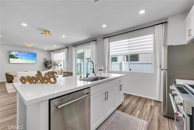kitchen featuring white cabinets, light wood-style flooring, a sink, an island with sink, and appliances with stainless steel finishes