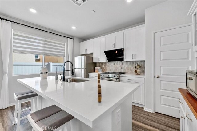 kitchen with dark wood-style floors, a sink, decorative backsplash, stainless steel appliances, and visible vents