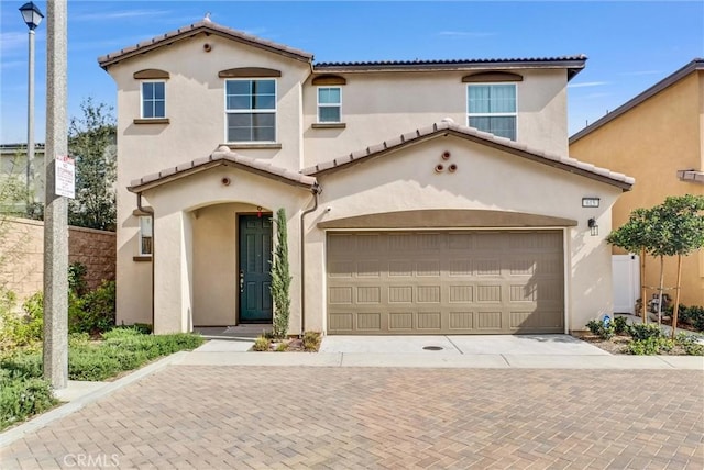 mediterranean / spanish-style house featuring decorative driveway, a tiled roof, fence, a garage, and stucco siding