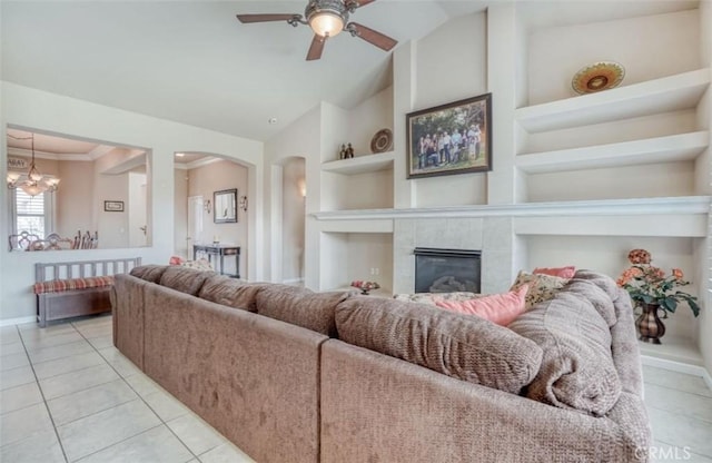living area with arched walkways, baseboards, built in features, ceiling fan with notable chandelier, and light tile patterned floors