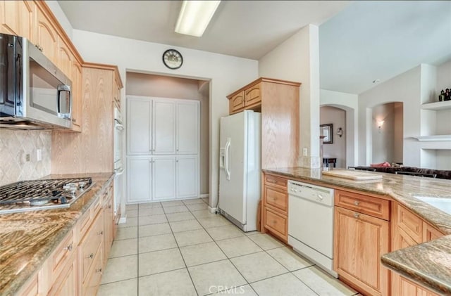 kitchen with light stone counters, arched walkways, backsplash, and appliances with stainless steel finishes