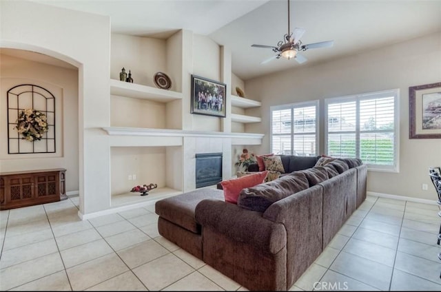 living room with baseboards, built in shelves, ceiling fan, a fireplace, and light tile patterned floors