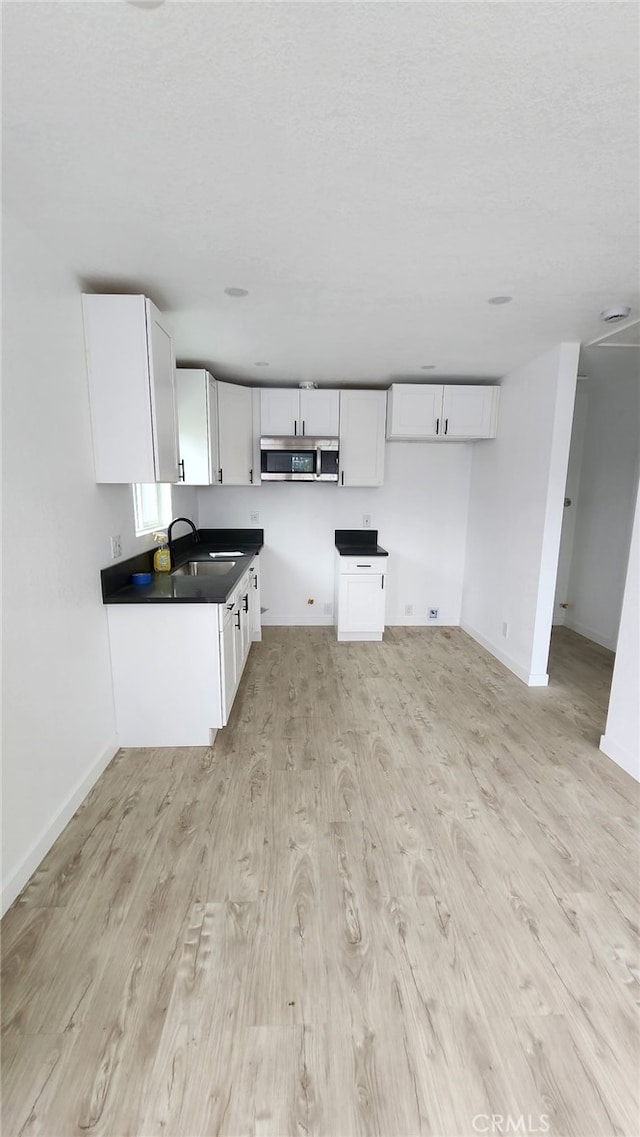 11114 Willowbrook Ave, Los Angeles, CA 90059 - kitchen featuring stainless steel microwave, light wood finished floors, white cabinets, and baseboards