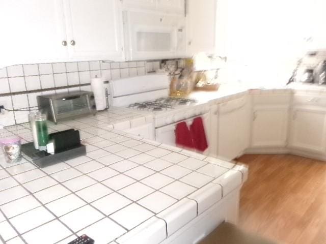 kitchen featuring white cabinets, light wood-style floors, decorative backsplash, white appliances, and tile countertops