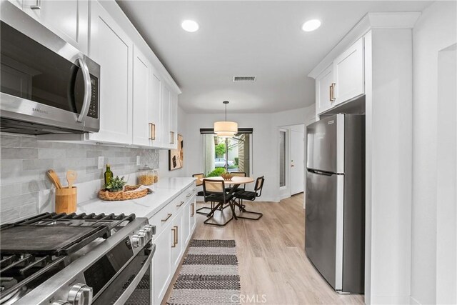 kitchen with visible vents, light wood-style floors, decorative backsplash, appliances with stainless steel finishes, and white cabinetry