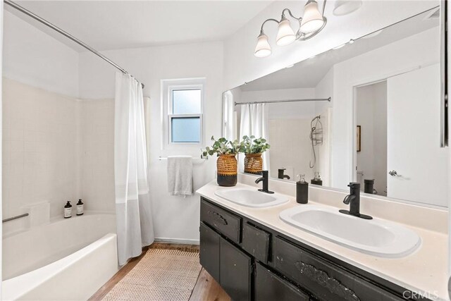 full bath featuring wood finished floors, a sink, shower / bathtub combination with curtain, and double vanity
