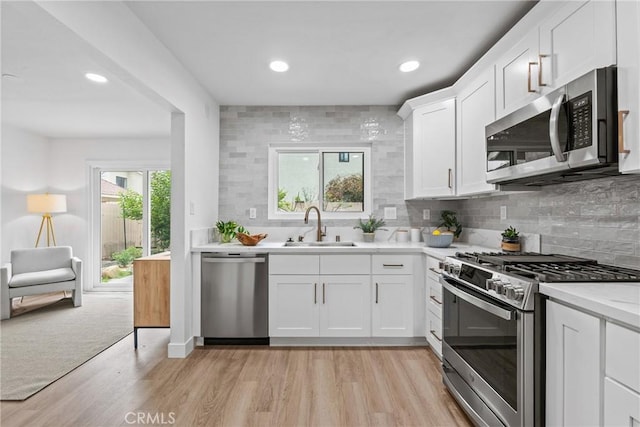 kitchen featuring a sink, backsplash, light wood-style floors, light countertops, and appliances with stainless steel finishes