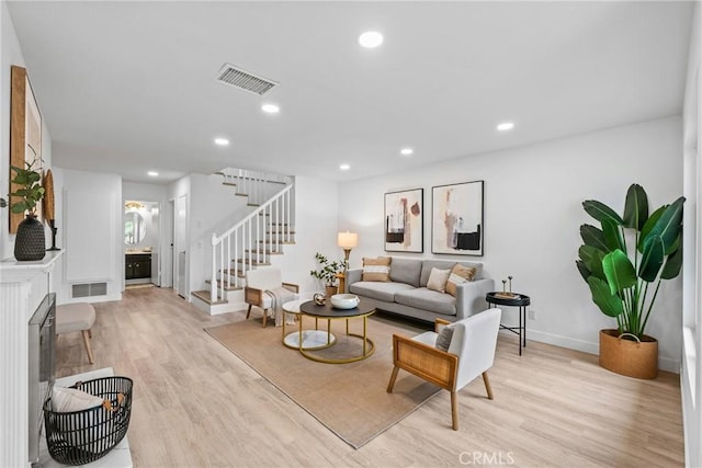 living area featuring baseboards, light wood-style flooring, visible vents, and stairs