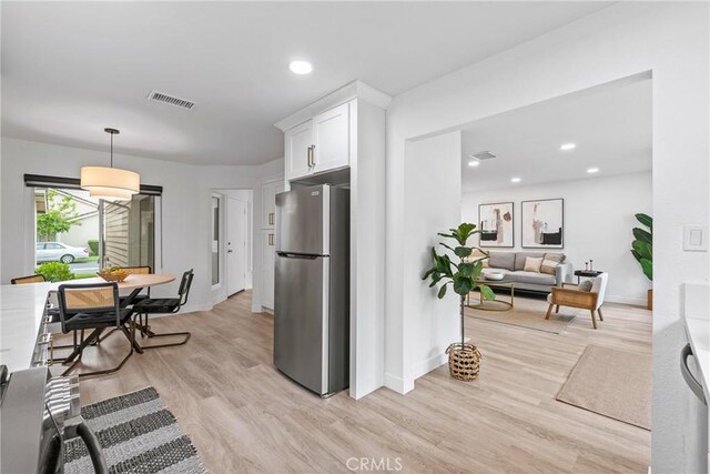 kitchen featuring white cabinets, visible vents, freestanding refrigerator, light wood-type flooring, and baseboards
