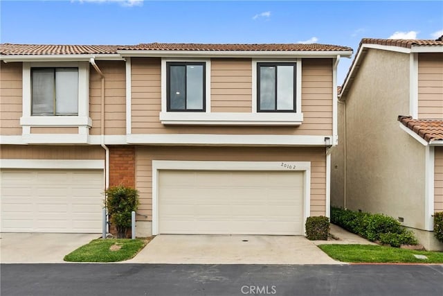 townhome / multi-family property featuring an attached garage, a tile roof, and driveway
