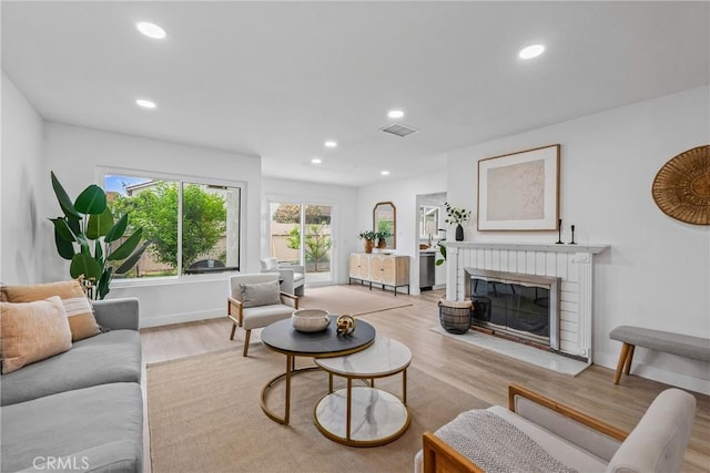 living room with recessed lighting, a brick fireplace, visible vents, and light wood-type flooring