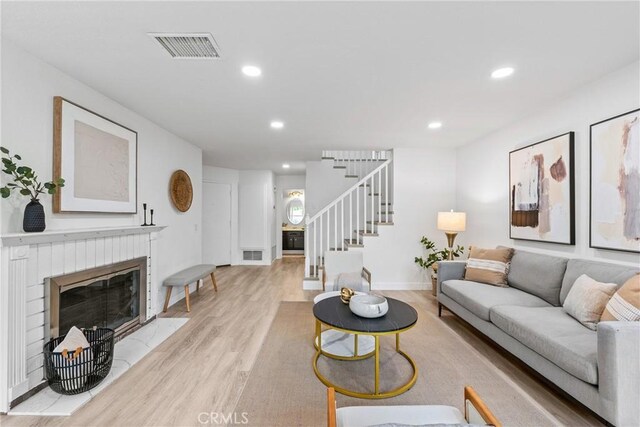living room featuring stairs, light wood-style floors, a brick fireplace, visible vents, and recessed lighting