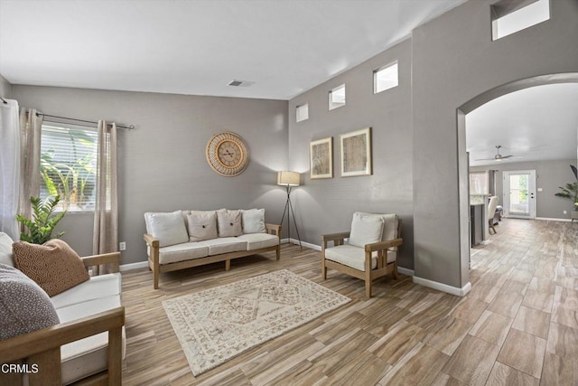 living area featuring light wood finished floors, arched walkways, visible vents, baseboards, and ceiling fan
