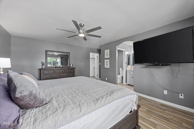 bedroom featuring arched walkways, baseboards, light wood-style floors, a ceiling fan, and ensuite bath