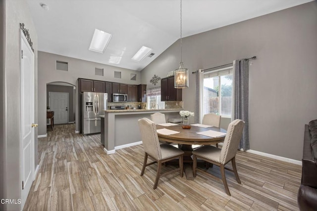 dining area featuring high vaulted ceiling, light wood-style floors, arched walkways, baseboards, and visible vents