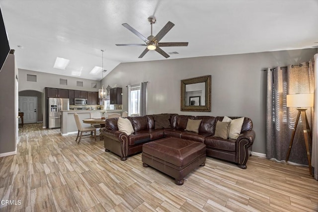 living room featuring arched walkways, lofted ceiling, a ceiling fan, and light wood-style flooring
