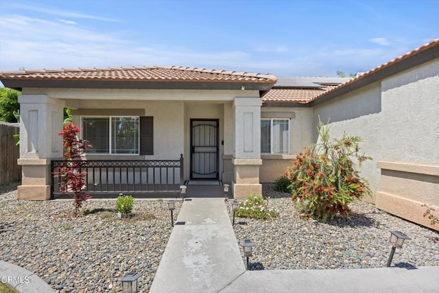 view of front of property with stucco siding, roof mounted solar panels, a tile roof, and covered porch