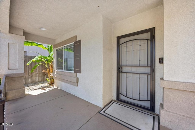view of exterior entry featuring stucco siding and fence