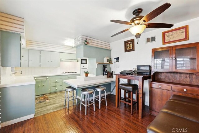 kitchen featuring visible vents, decorative backsplash, wood finished floors, ceiling fan, and stovetop