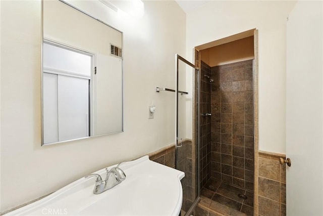 bathroom featuring a sink, a tile shower, tile walls, wainscoting, and visible vents