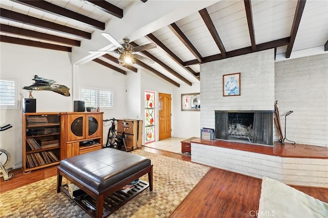 living room featuring wood finished floors, a brick fireplace, a ceiling fan, and lofted ceiling with beams