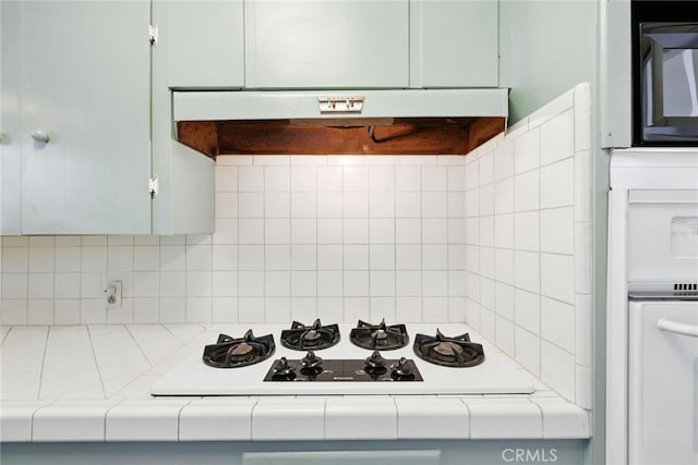 kitchen featuring white gas cooktop, backsplash, black microwave, under cabinet range hood, and tile countertops