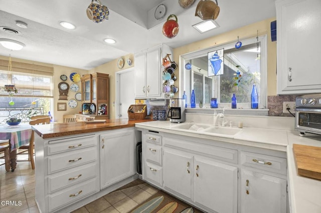 kitchen featuring tile patterned flooring, a peninsula, wood counters, and a sink