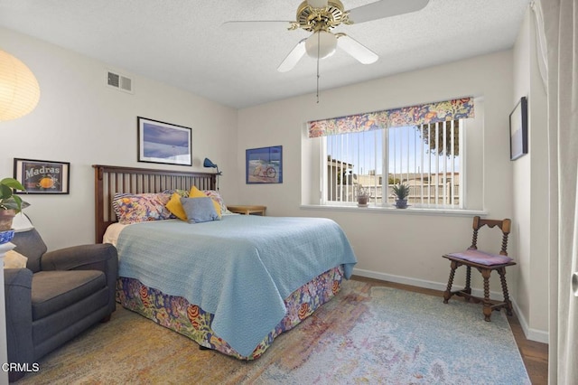 bedroom featuring a textured ceiling, baseboards, visible vents, wood finished floors, and ceiling fan