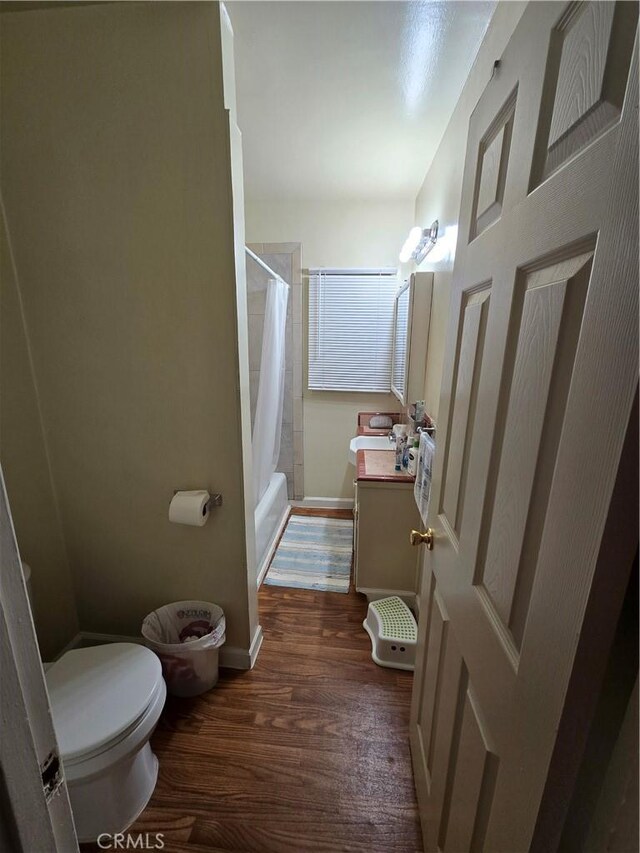bathroom with vanity, wood finished floors, shower / bath combination with curtain, toilet, and baseboards