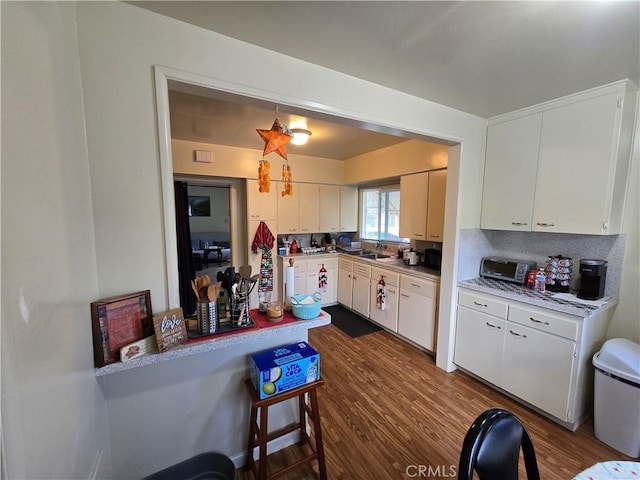 kitchen with a sink, light countertops, dark wood finished floors, and white cabinetry