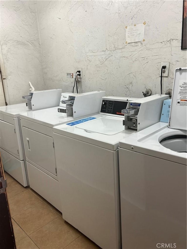 shared laundry area with light tile patterned flooring, a textured wall, and washing machine and clothes dryer