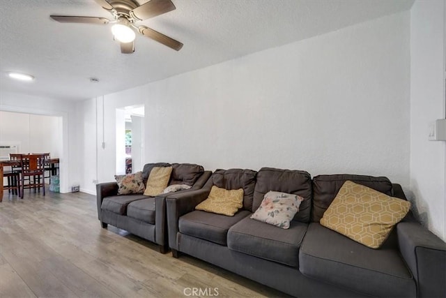living room featuring baseboards, a ceiling fan, wood finished floors, and a textured ceiling