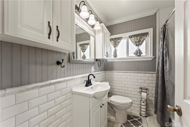 bathroom with wainscoting, toilet, tile patterned floors, vanity, and ornamental molding