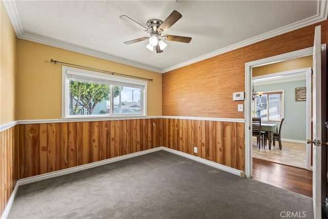empty room with healthy amount of natural light, a ceiling fan, wooden walls, ornamental molding, and wainscoting