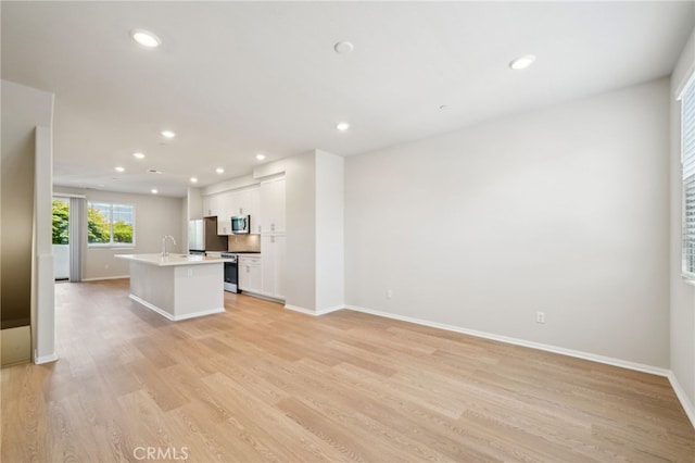 219 Aurora Ln, Pomona, CA 91767 - kitchen with appliances with stainless steel finishes, an island with sink, white cabinetry, light wood finished floors, and baseboards