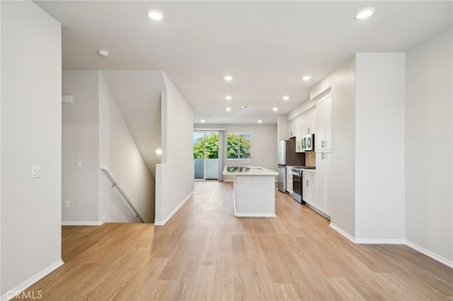 219 Aurora Ln, Pomona, CA 91767 - kitchen featuring stainless steel appliances, white cabinets, light wood-style floors, a kitchen island with sink, and light countertops