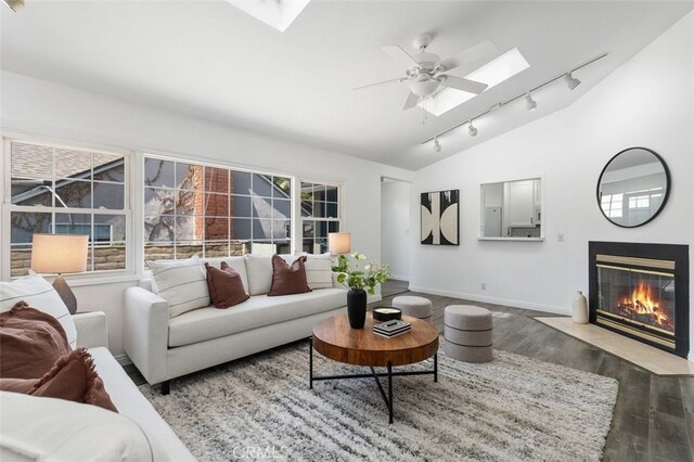 living area featuring lofted ceiling with skylight, wood finished floors, track lighting, a fireplace with flush hearth, and baseboards