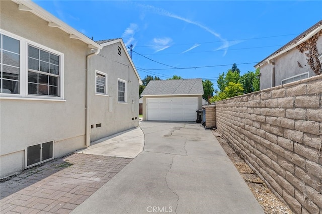 view of side of home featuring a garage, an outdoor structure, fence, and stucco siding