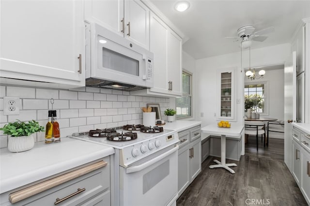 kitchen with light countertops, white appliances, dark wood-type flooring, decorative backsplash, and ceiling fan with notable chandelier