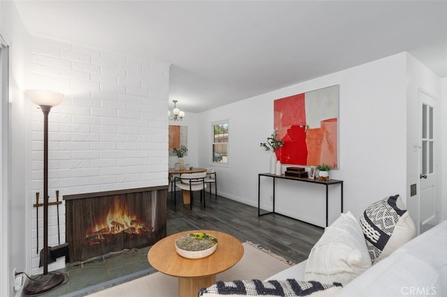 living room featuring wood finished floors, a brick fireplace, and an inviting chandelier