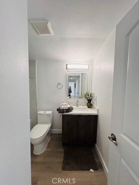 bathroom featuring vanity, toilet, visible vents, baseboards, and wood finished floors