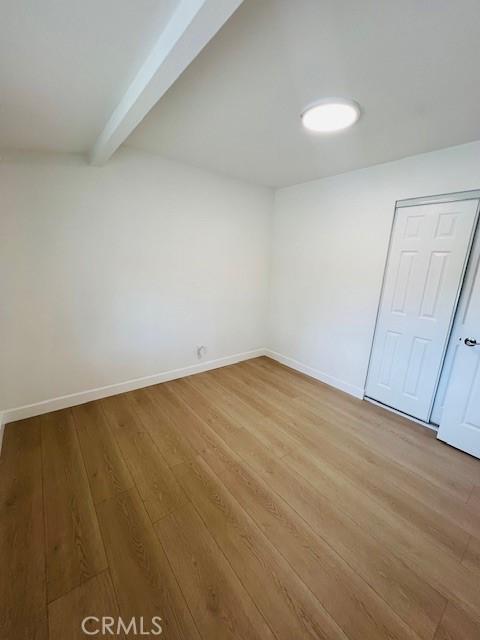 empty room with beam ceiling, light wood finished floors, and baseboards